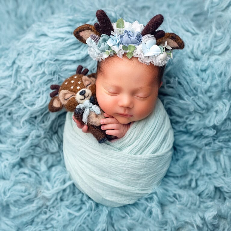 Newborn focení v bílé zavinovačce s čepičkou na modrém pozadí - fotograf elena Parfinchuk