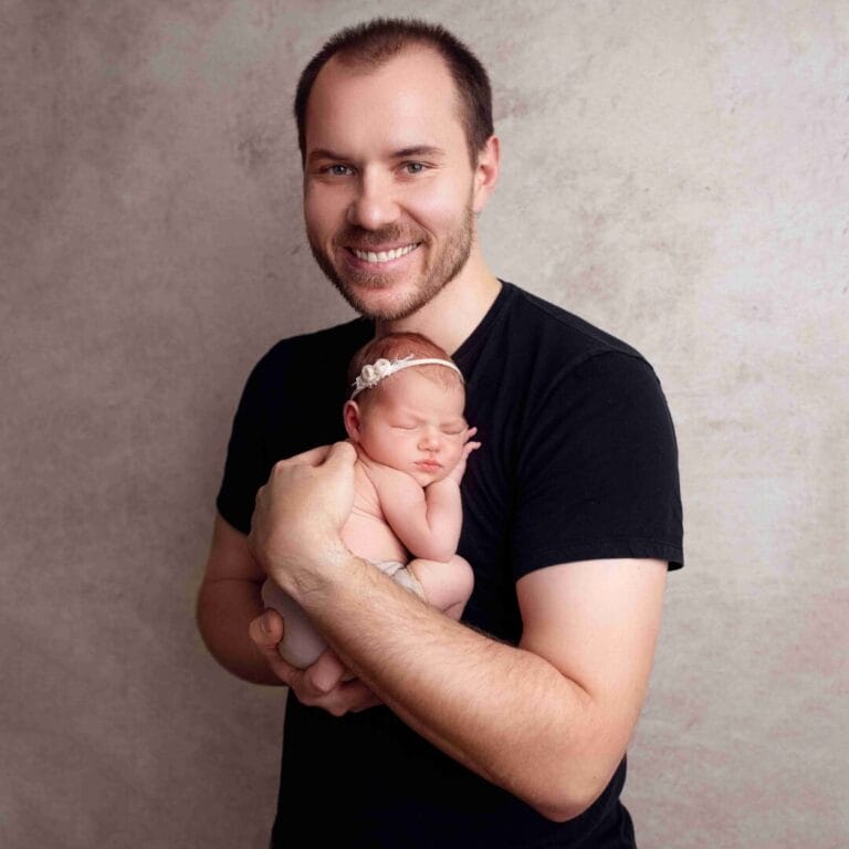 Tatínek s miminkem: „Rodinné newborn focení Praha, portrét usmívajícího se tatínka držícího své novorozené miminko v náručí.“