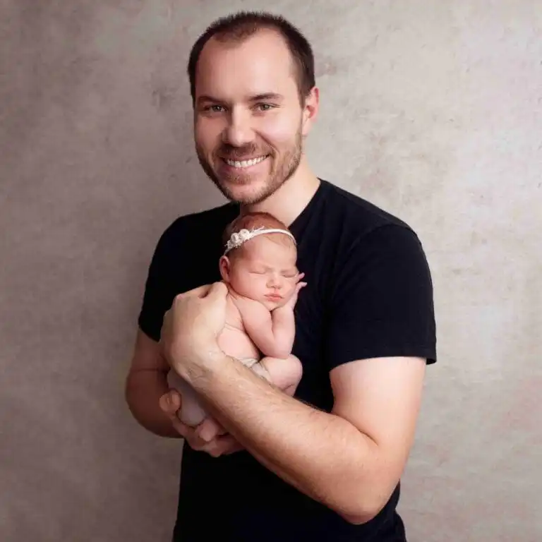 Tatínek s miminkem: „Rodinné newborn focení Praha, portrét usmívajícího se tatínka držícího své novorozené miminko v náručí.“
