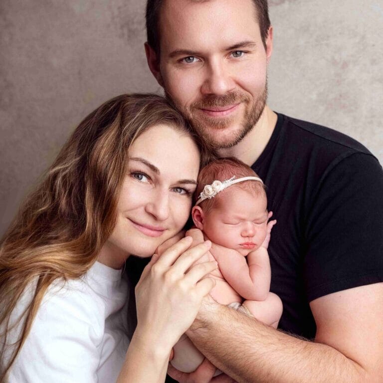 Rodiče s miminkem: „Lifestylové newborn focení v Praze, usmívající se rodiče s miminkem v náručí v profesionálním ateliéru.“