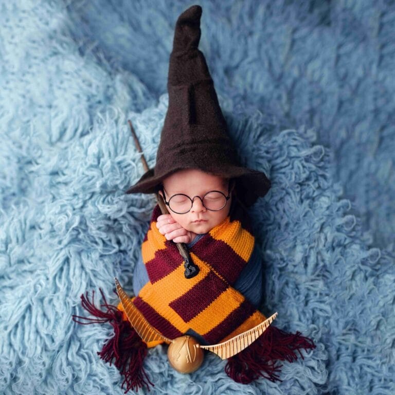 Harry Potter (detail šály): „Umělecké newborn focení v Praze, miminko s rekvizitami kouzelnické hůlky a nebelvírské šály na modrém pozadí.“