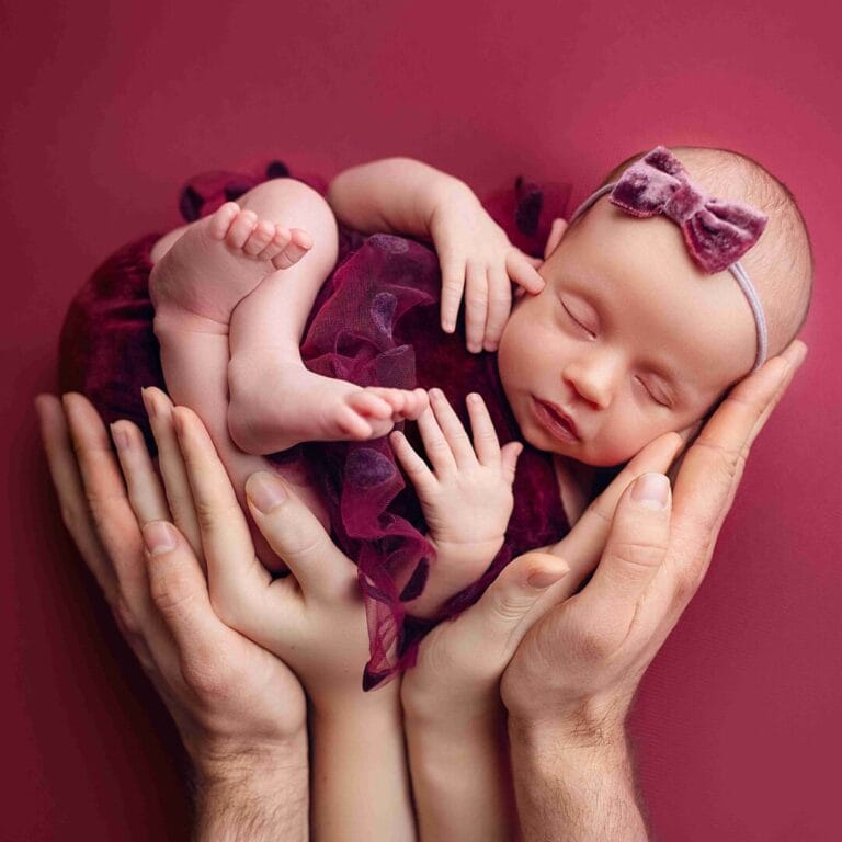 Newborn focení, miminko v dlaních rodičů na vínovém pozadí