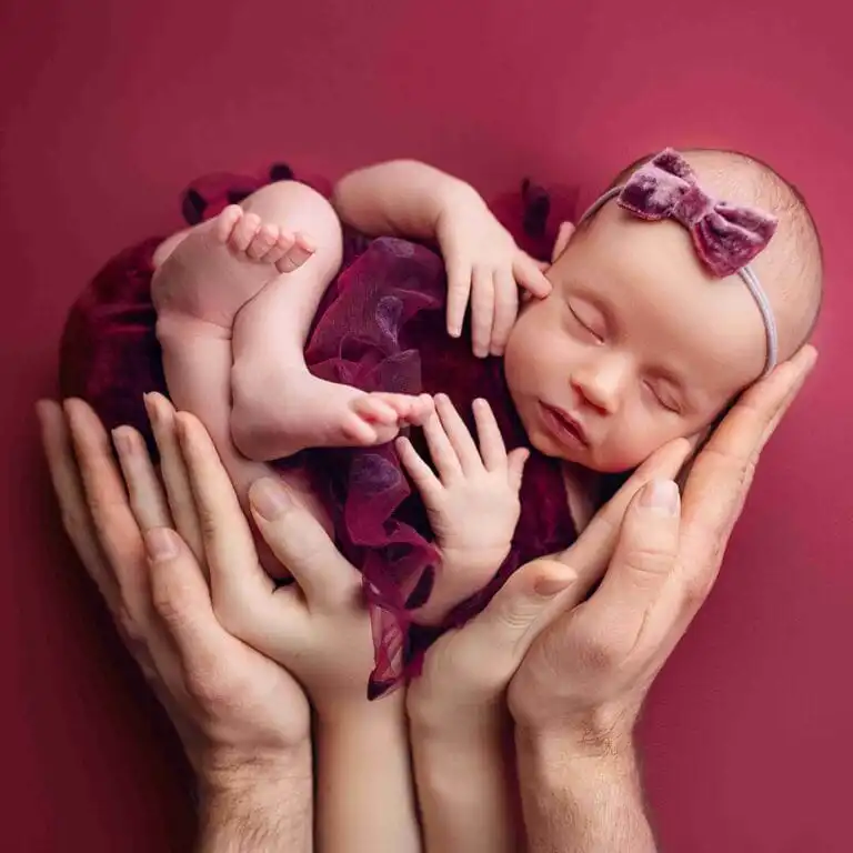 Newborn focení, miminko v dlaních rodičů na vínovém pozadí